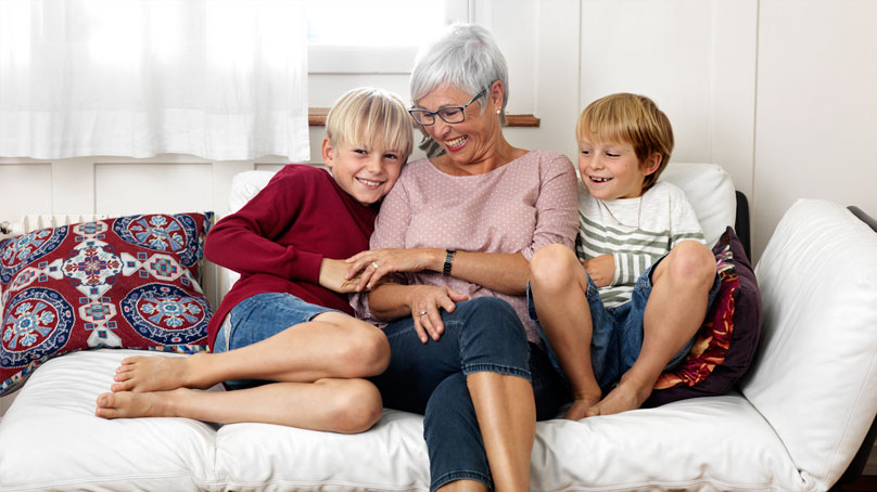 Eine glückliche Seniorin sitzt mit ihren zwei Enkelkinder auf dem Sofa