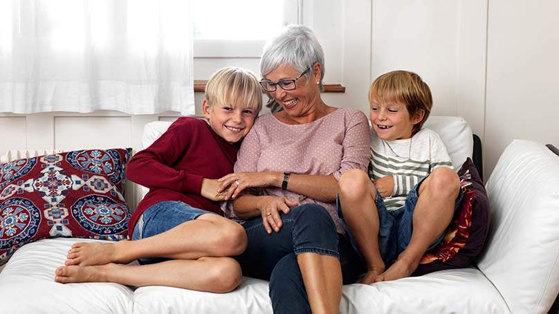 Seniorin sitzt mit ihren Enkeln gemütlich auf dem Sofa